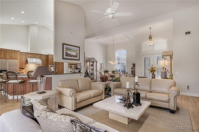 living area featuring baseboards, recessed lighting, a towering ceiling, ceiling fan with notable chandelier, and light wood-type flooring