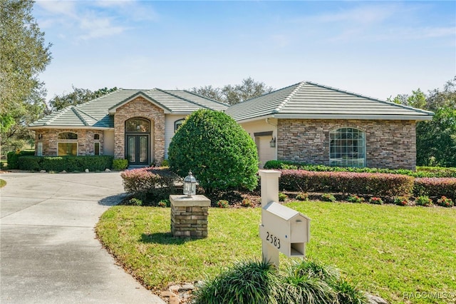 ranch-style house with a tiled roof, an attached garage, french doors, and a front lawn