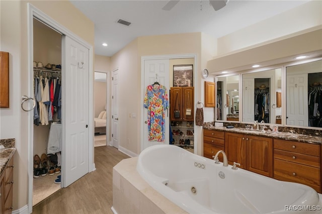 bathroom featuring a spacious closet, ceiling fan, a whirlpool tub, wood finished floors, and vanity