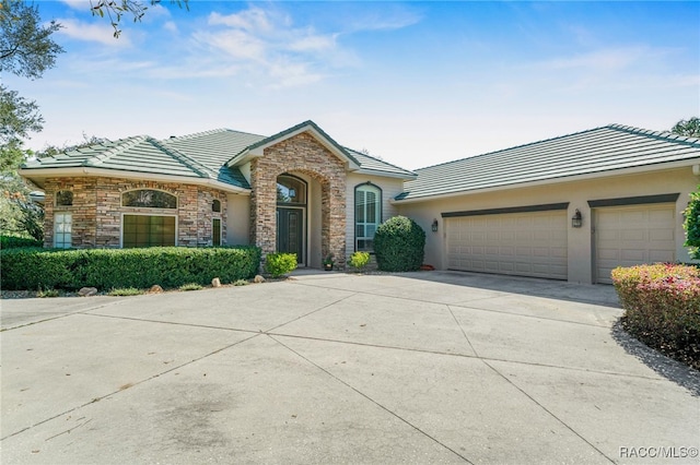 single story home with a tiled roof, stone siding, driveway, and stucco siding