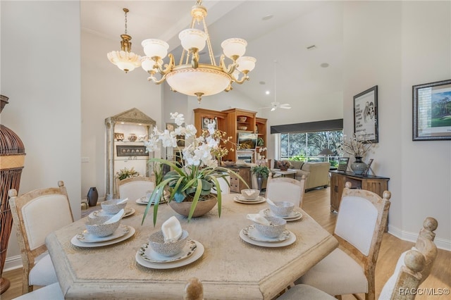 dining space featuring light wood-style flooring, ceiling fan with notable chandelier, a high ceiling, and baseboards