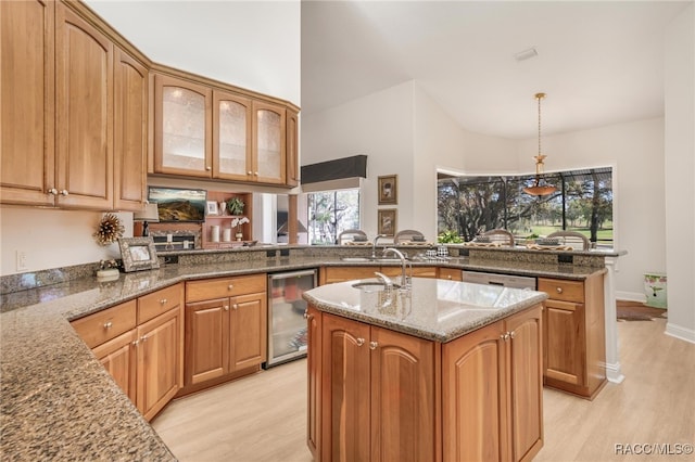 kitchen with wine cooler, stone counters, a center island with sink, and light wood-type flooring