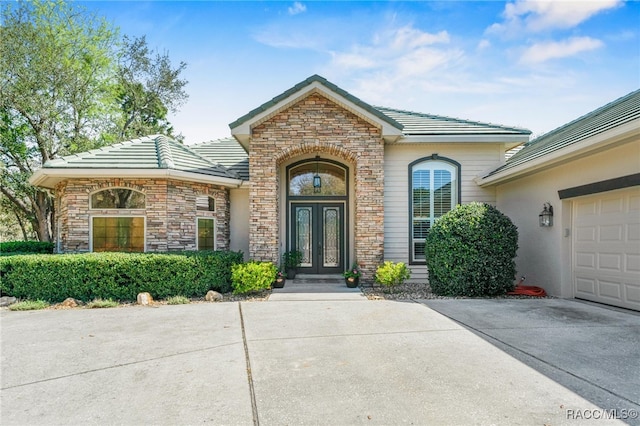 doorway to property with a tiled roof, an attached garage, french doors, and stone siding