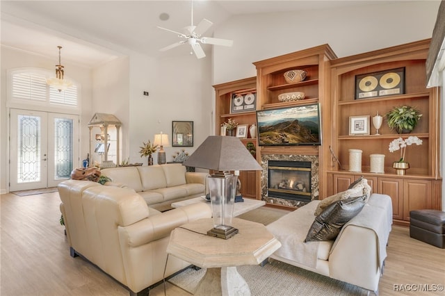 living room with light wood-type flooring, high vaulted ceiling, a premium fireplace, and a ceiling fan