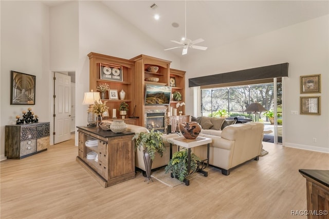 living area with a glass covered fireplace, a ceiling fan, light wood finished floors, and high vaulted ceiling