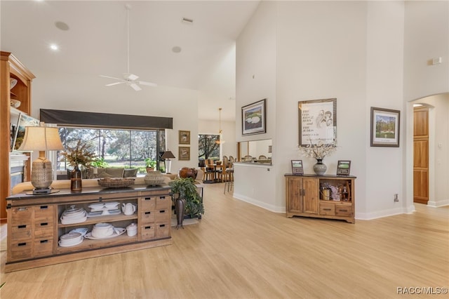 living room featuring arched walkways, light wood-style flooring, a high ceiling, and a ceiling fan