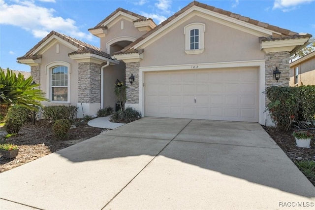 mediterranean / spanish house with an attached garage, stone siding, concrete driveway, a tiled roof, and stucco siding