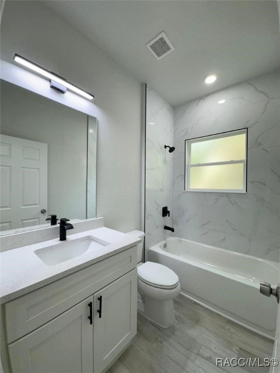 full bathroom featuring vanity, tiled shower / bath combo, and toilet