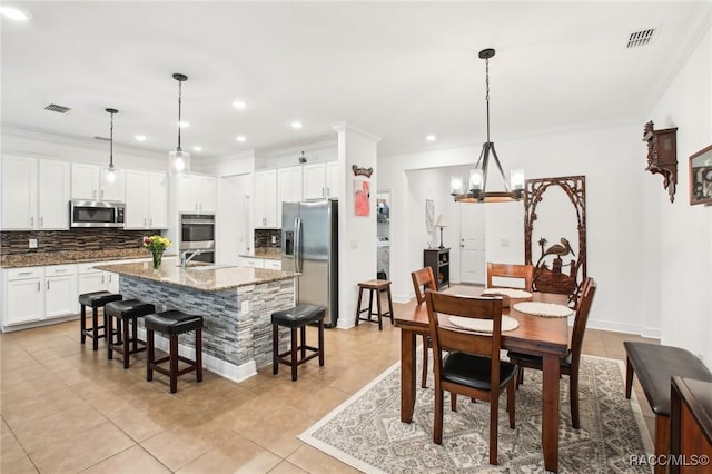 kitchen featuring a breakfast bar area, a center island with sink, appliances with stainless steel finishes, pendant lighting, and dark stone counters