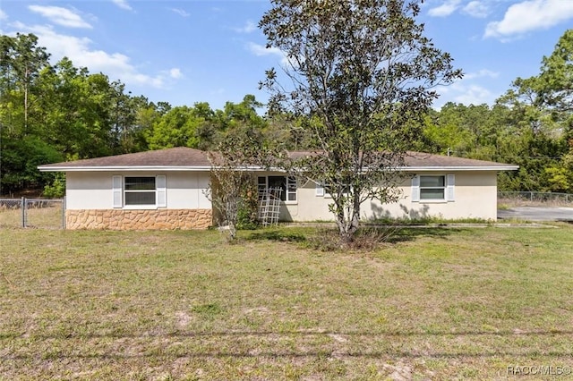 view of front of property with a front yard, stucco siding, fence, and stone siding