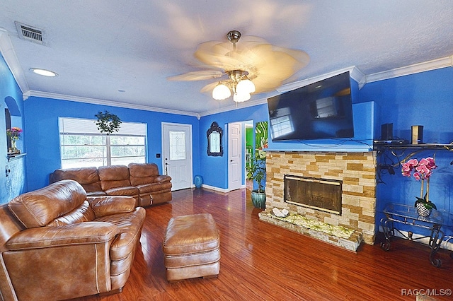 living room with ceiling fan, a stone fireplace, wood-type flooring, and crown molding