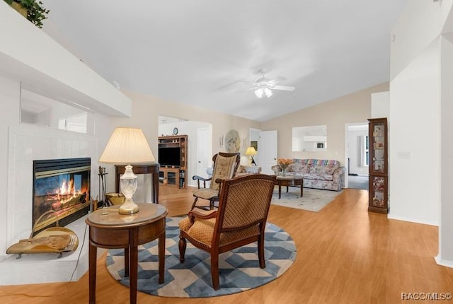 living area featuring light wood-type flooring, vaulted ceiling, ceiling fan, and a tiled fireplace