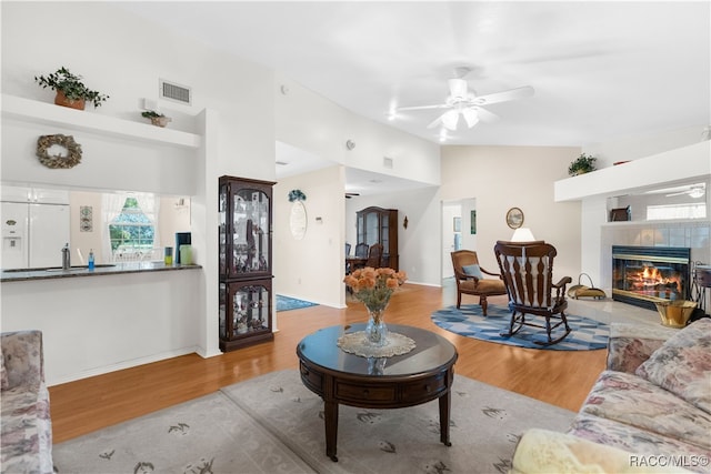 living room with a tiled fireplace, ceiling fan, light hardwood / wood-style flooring, and vaulted ceiling