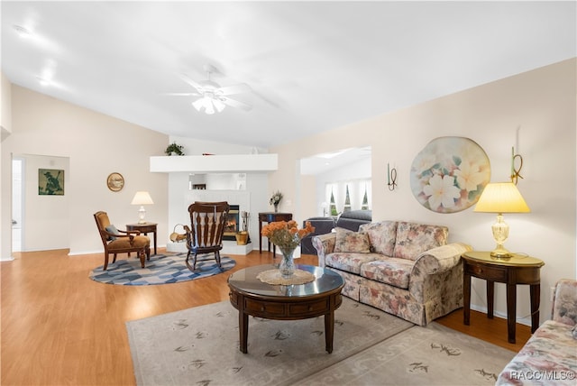 living room with ceiling fan, light hardwood / wood-style floors, and vaulted ceiling