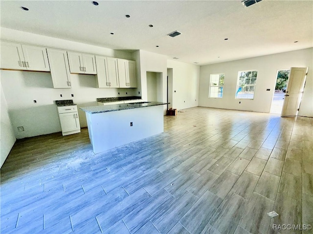 kitchen with dark stone counters, a center island, light hardwood / wood-style flooring, and white cabinets