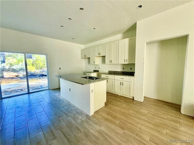 kitchen featuring white cabinetry, light wood-type flooring, dark stone countertops, and a kitchen island