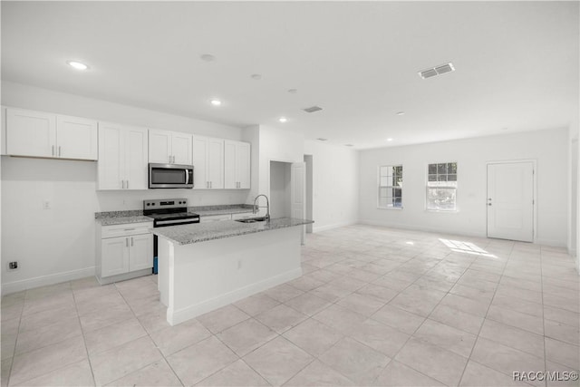 kitchen featuring sink, appliances with stainless steel finishes, light stone countertops, an island with sink, and white cabinets