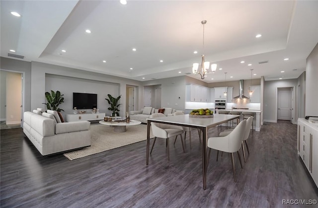 dining room with a tray ceiling, dark hardwood / wood-style floors, and an inviting chandelier