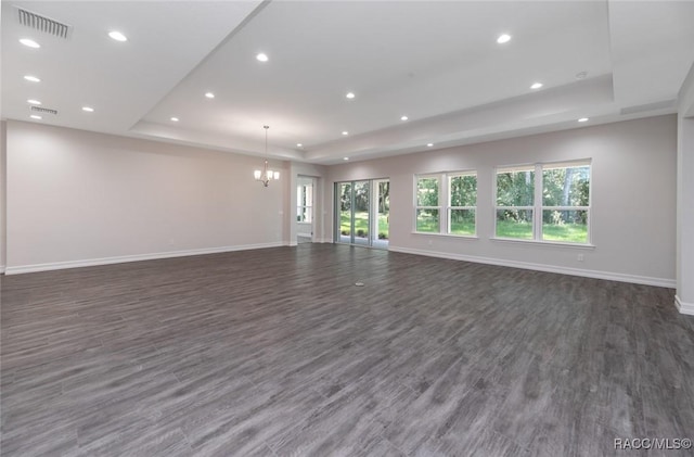 unfurnished living room featuring an inviting chandelier, dark hardwood / wood-style flooring, and a tray ceiling