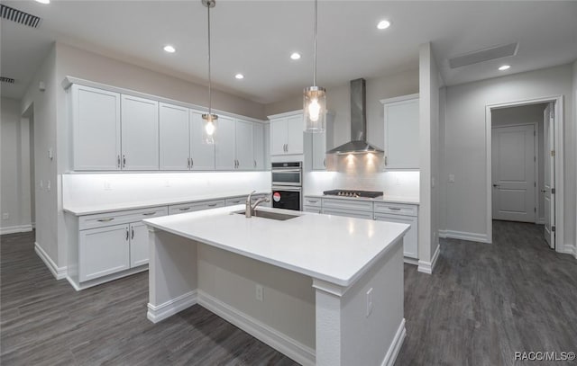 kitchen featuring white cabinets, sink, a kitchen island with sink, and wall chimney range hood