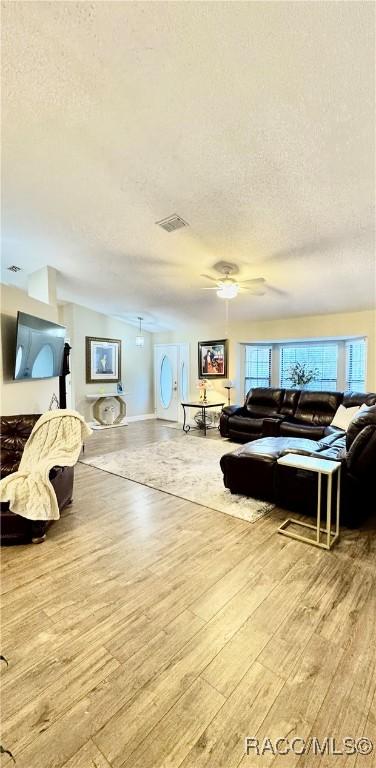 living room featuring a textured ceiling, ceiling fan, and light wood-type flooring