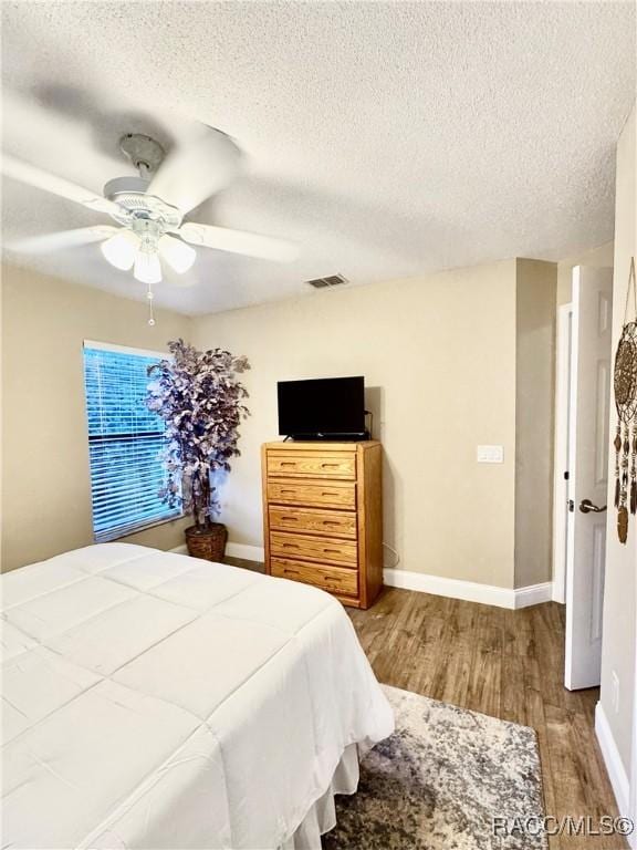 bedroom with ceiling fan, wood-type flooring, and a textured ceiling