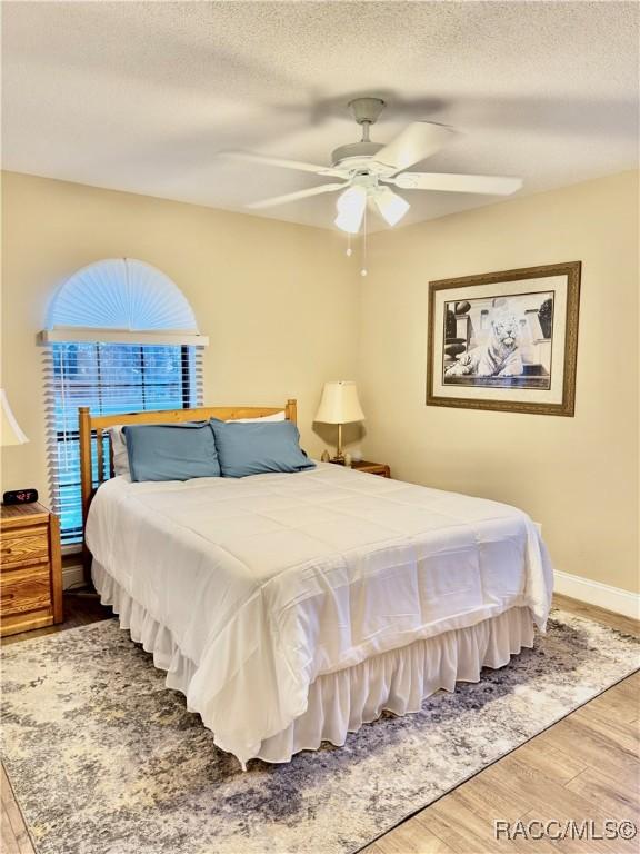 bedroom with a textured ceiling, ceiling fan, and hardwood / wood-style flooring