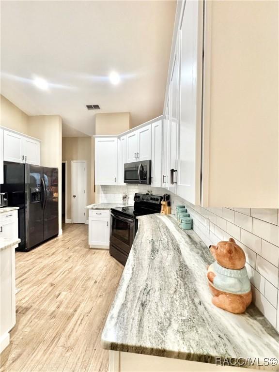 kitchen featuring white cabinetry, backsplash, light stone counters, and black appliances