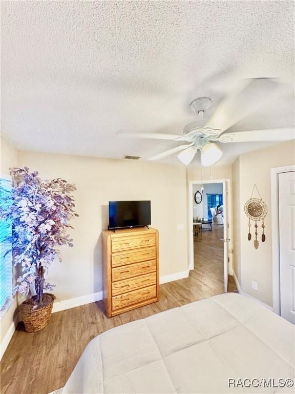 bedroom with a textured ceiling, ceiling fan, and hardwood / wood-style floors