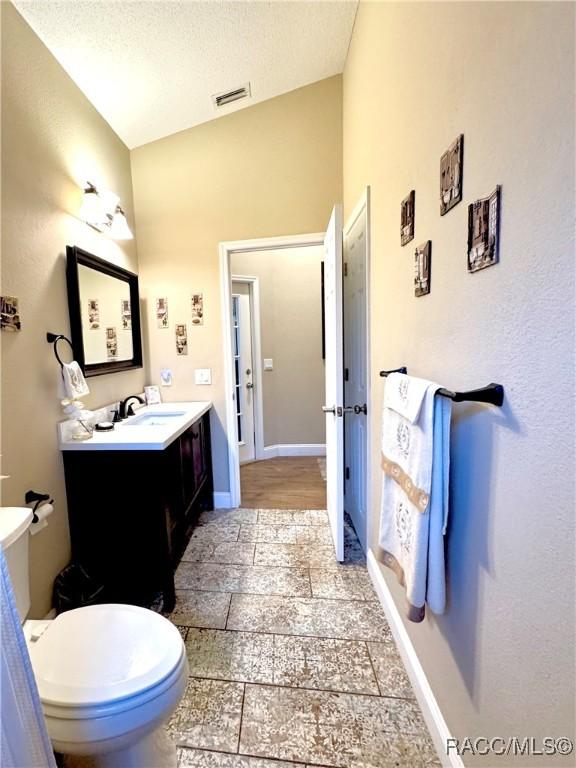 bathroom featuring a textured ceiling, toilet, vanity, and vaulted ceiling