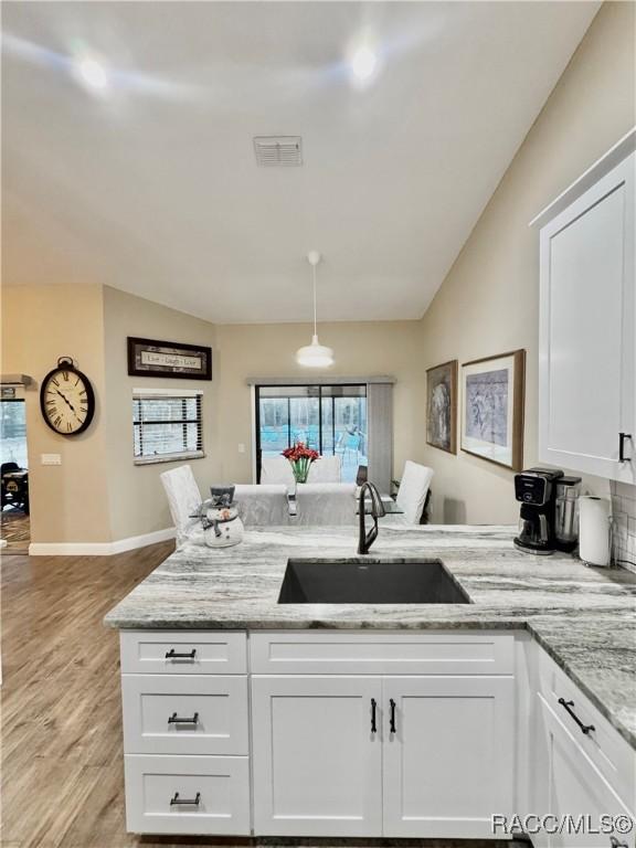 kitchen with vaulted ceiling, sink, light stone counters, and white cabinetry