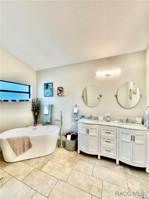 bathroom featuring lofted ceiling, vanity, tile patterned floors, a bathing tub, and a textured ceiling