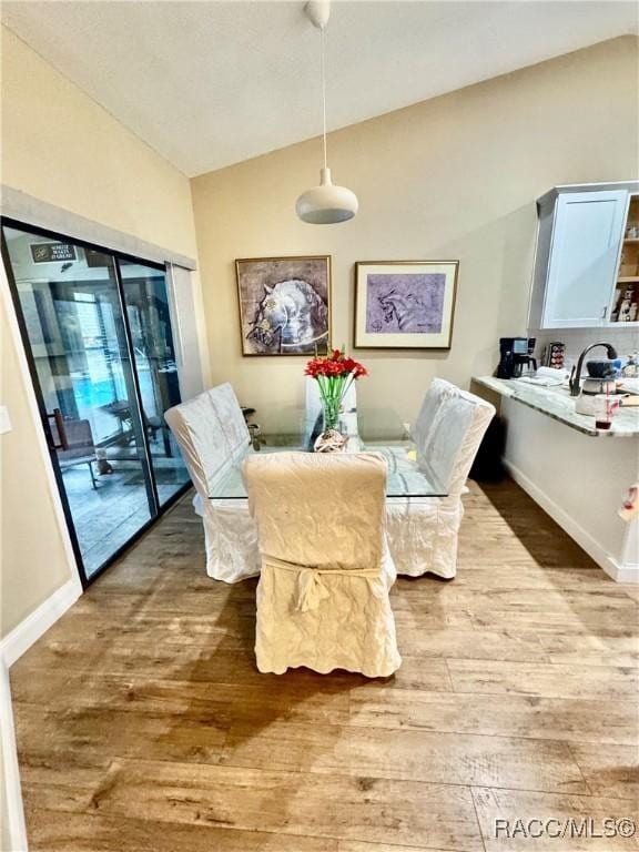 dining area featuring lofted ceiling, hardwood / wood-style flooring, and sink