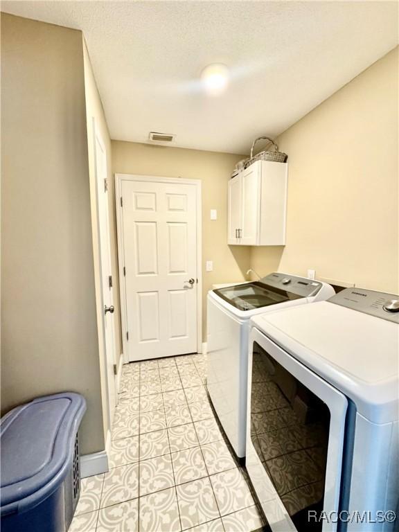 laundry room featuring washer and dryer, cabinets, and light tile patterned flooring