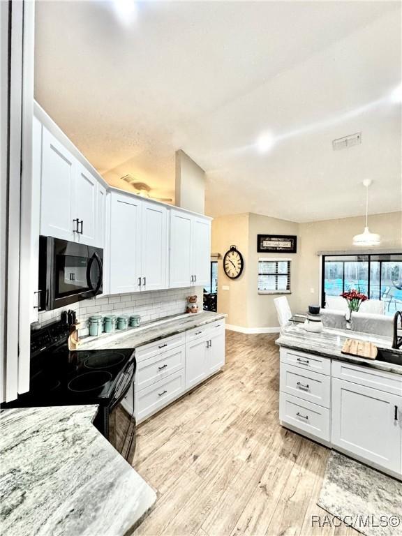 kitchen with white cabinets, black appliances, tasteful backsplash, light stone counters, and light hardwood / wood-style flooring