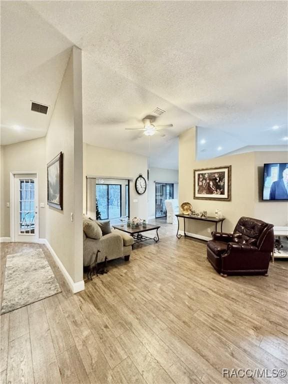 living room featuring light wood-type flooring, ceiling fan, lofted ceiling, and a textured ceiling