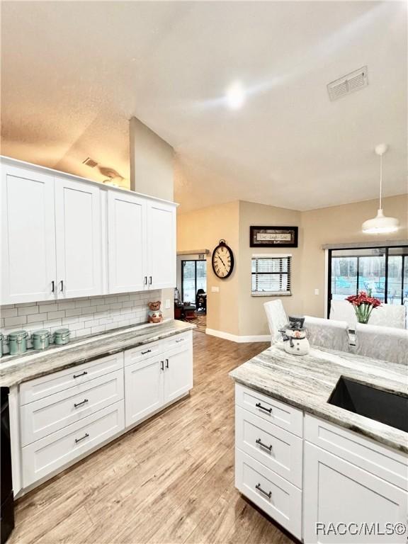 kitchen with light wood-type flooring, decorative backsplash, white cabinets, and pendant lighting