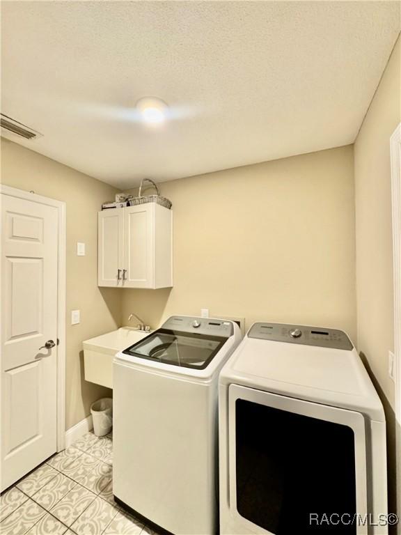 laundry area with a textured ceiling, cabinets, sink, independent washer and dryer, and light tile patterned flooring