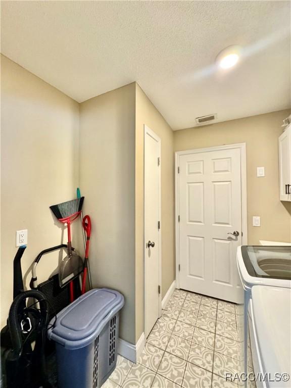 washroom with light tile patterned floors, separate washer and dryer, a textured ceiling, and cabinets