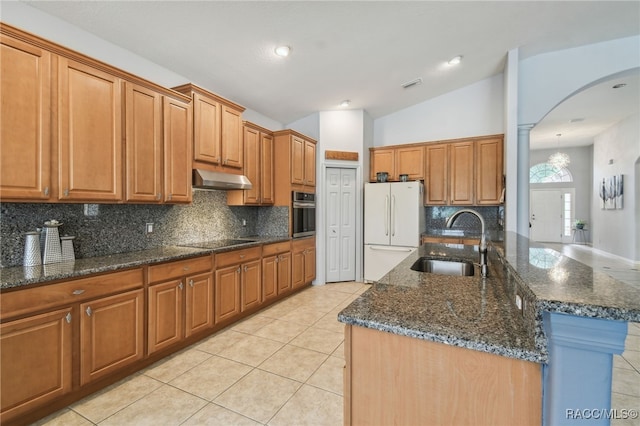 kitchen featuring lofted ceiling, black electric stovetop, sink, dark stone countertops, and white fridge