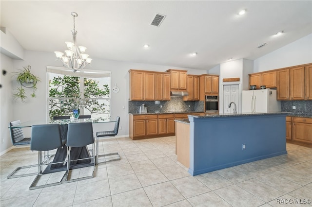 kitchen featuring tasteful backsplash, vaulted ceiling, a kitchen island with sink, an inviting chandelier, and white fridge