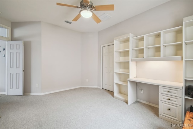 unfurnished office with ceiling fan, light colored carpet, and built in desk