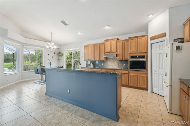 kitchen with stainless steel oven, a kitchen island with sink, white refrigerator, lofted ceiling, and decorative backsplash