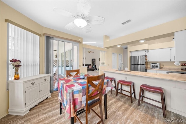 dining space with ceiling fan, sink, and light wood-type flooring