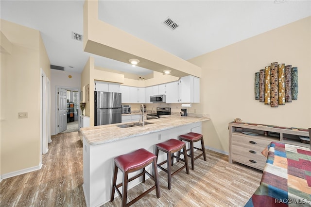 kitchen with a kitchen breakfast bar, stainless steel appliances, sink, light hardwood / wood-style flooring, and white cabinets