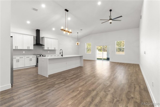 kitchen with a kitchen island with sink, wall chimney range hood, appliances with stainless steel finishes, decorative light fixtures, and white cabinetry