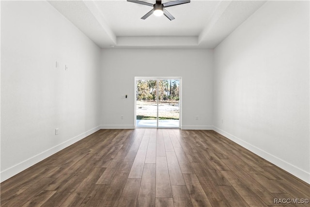 empty room featuring a raised ceiling, ceiling fan, and dark hardwood / wood-style floors