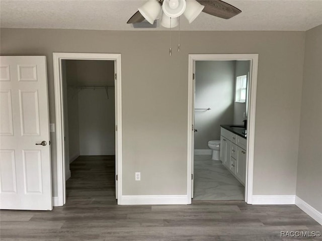 unfurnished bedroom with hardwood / wood-style floors, ensuite bath, a spacious closet, and ceiling fan