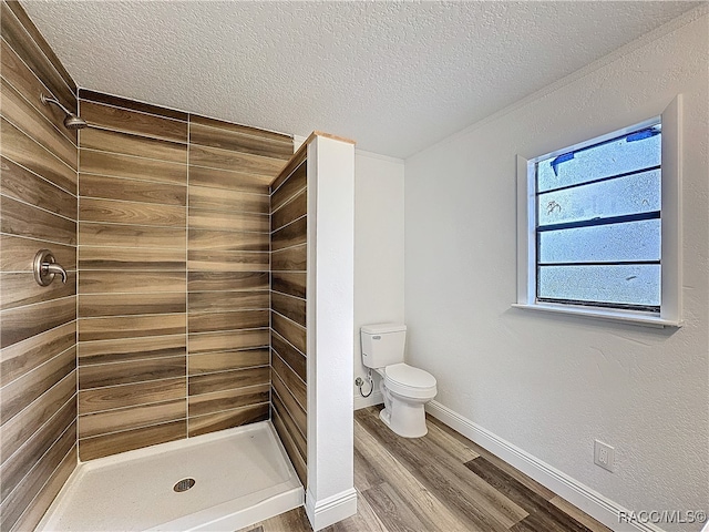 bathroom with a stall shower, baseboards, toilet, wood finished floors, and a textured ceiling