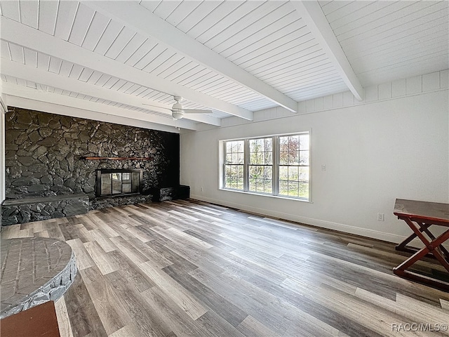 living room with beamed ceiling, a stone fireplace, baseboards, and wood finished floors